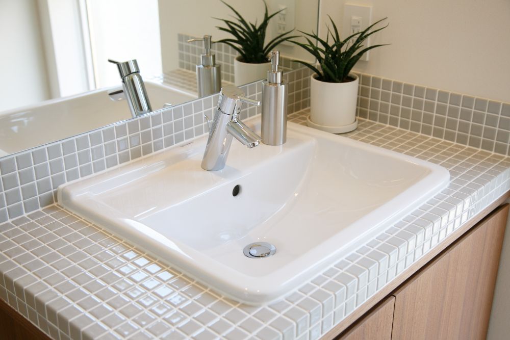 ライトグレーのタイルと白い洗面器で造られたシンプルな洗面